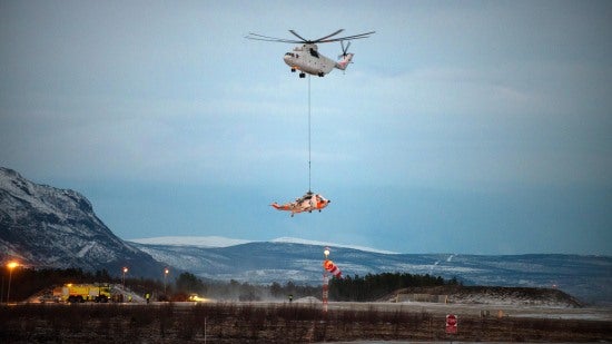 A Mil MI-26 helicopter airlifting a str和ed Sea King helicopter in the Arctic Circle.