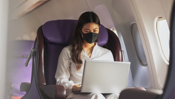 Деловая женщина в маске работает на ноутбуке в самолете