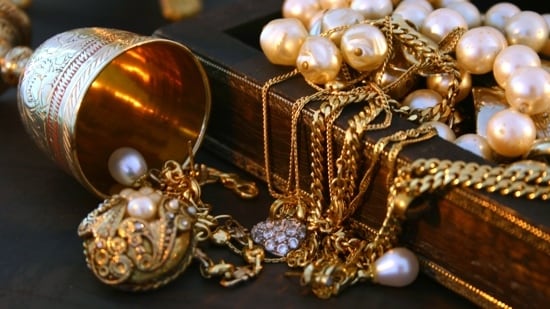 A golden goblet next to a small chest filled with gold chains and pearl necklaces.