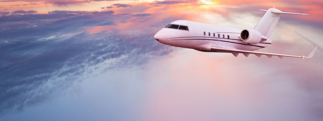 a private jet ascending higher into the sky above the clouds during sunset