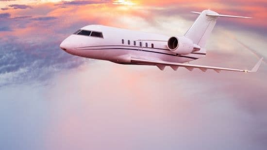 A private jet ascending higher into the sky above the clouds during sunset