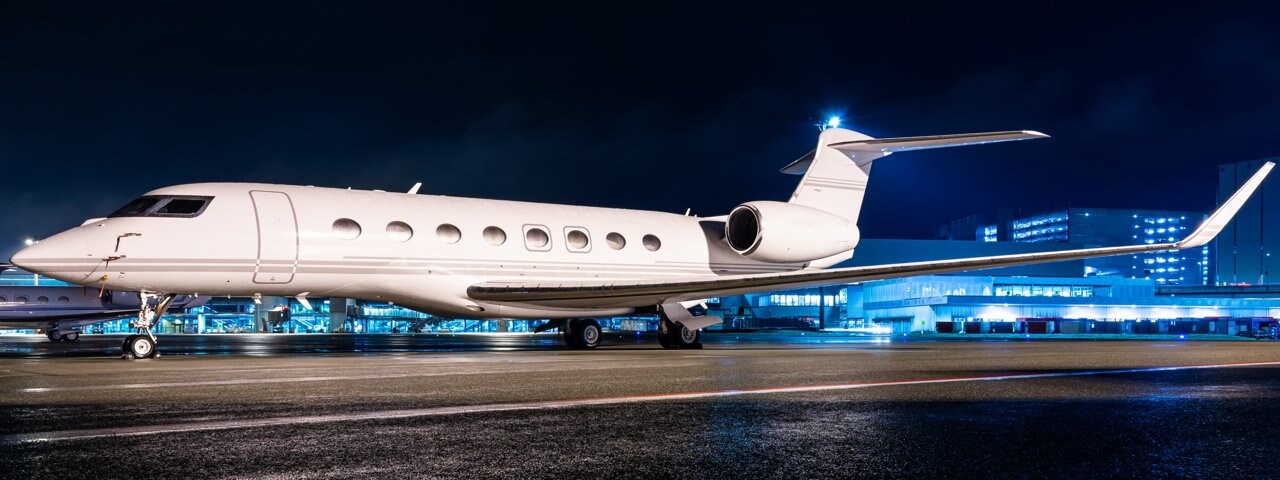 A private jet parked on the tarmac near an airport building at night.