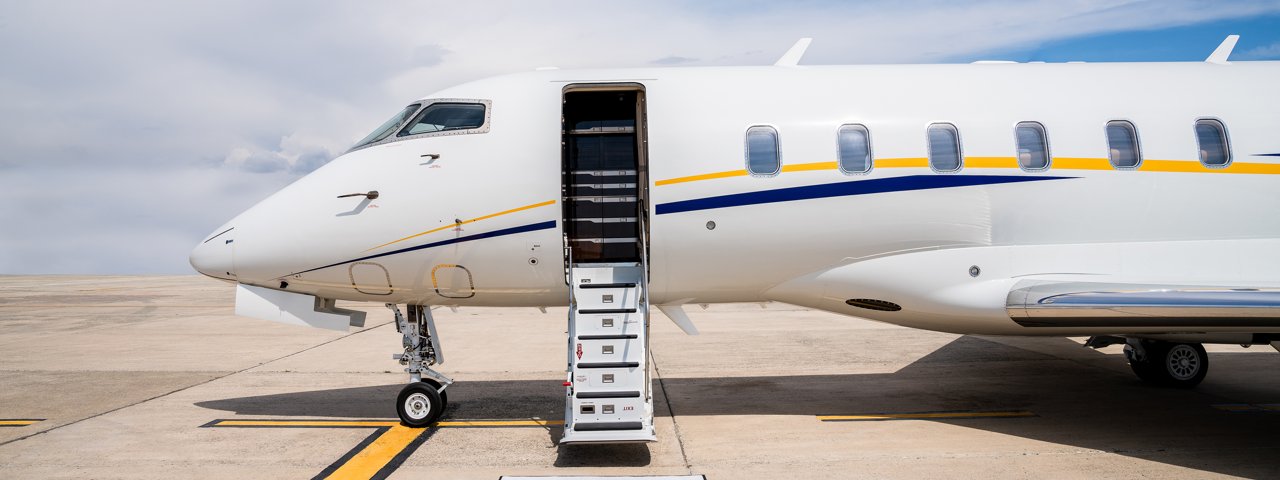 A view of the front half of a private jet with its stairs down parked on the tarmac.