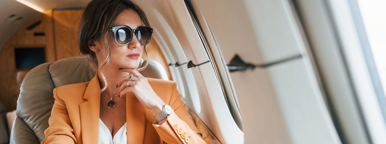 A well-dressed woman looking out of the window of a private jet.