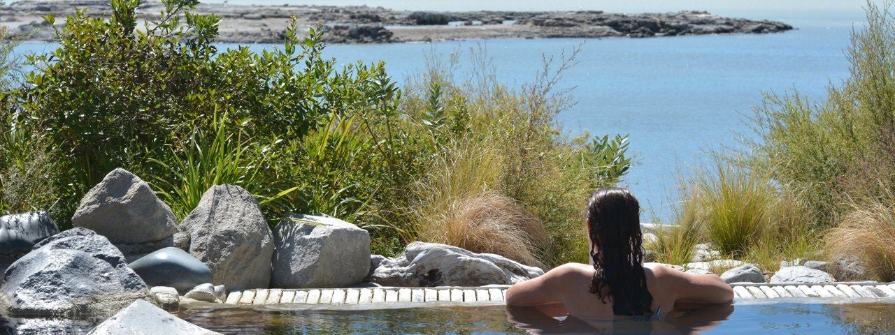 A woman in a hot pool in Rotorua, New Zealand, looks out across a nearby lake.