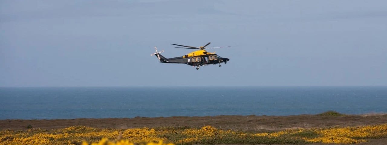 An AgustaWestland AW109 Grand comes in to land in a field with yellow flowers.