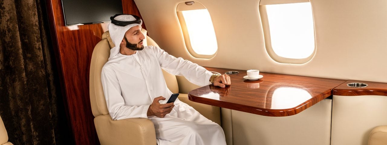 An Arabic businessman sitting on a private jet with his phone in his hand.