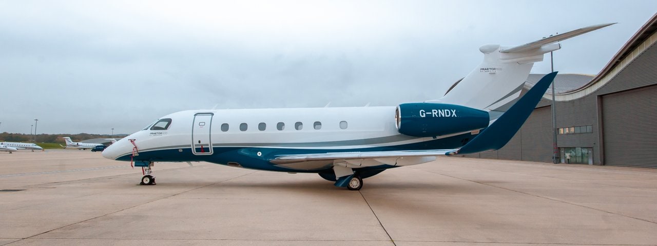 An Embraer Praetor 600 parked on the tarmac outside a hangar.