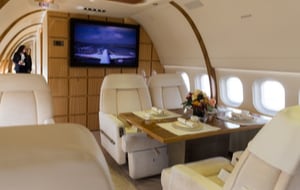 Luxurious interior of a private plane with seats around a table and a flatscreen in the background.