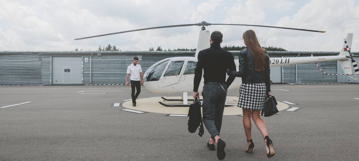Young fashionable couple walk to meet pilot at white private helicopter
