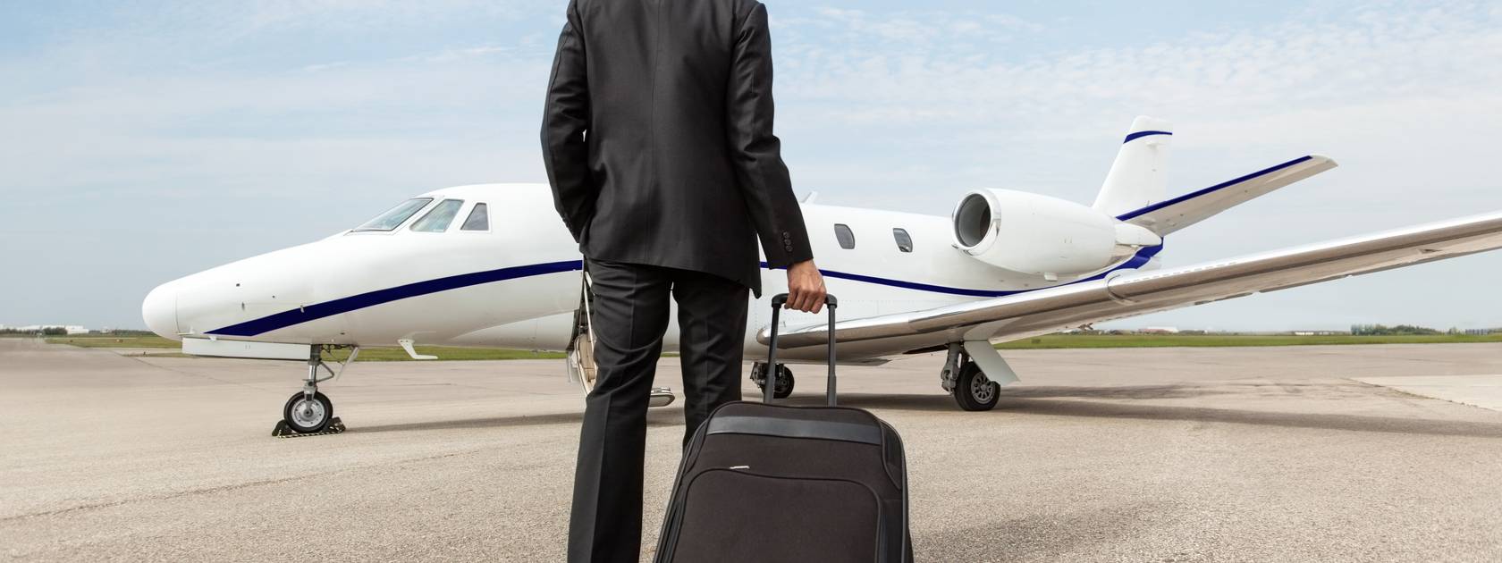 Man walking towards private jet on a runway while dragging a suitcase