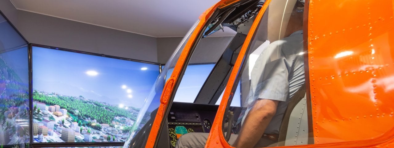 VR helicopter training for young pilots in an orange helicopter simulator.