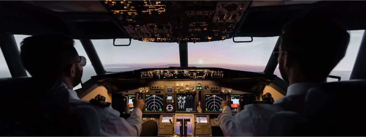 Back view of two pilots flying a commercial airplane into the sunset.