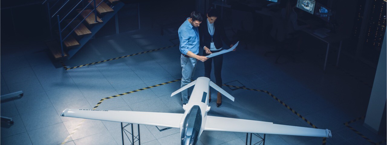 Two aerospace engineers looking over plans in front of a model airplane.