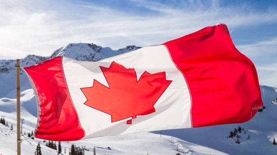 The Canadian flag waving with snowy mountains in the background.