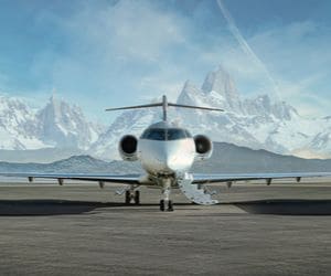 A private jet parked on a runway against a backdrop of snow-covered mountains