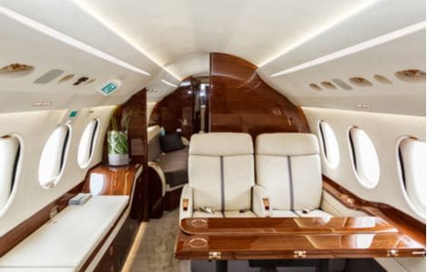 The interior of a luxury jet with plush cream seats and a wooden table and panelling