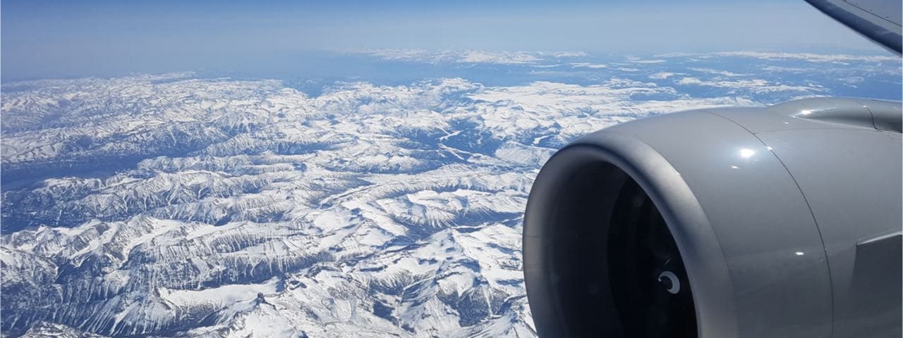 A picture of snow covered mountains from an airplane window with the props in the foreground.