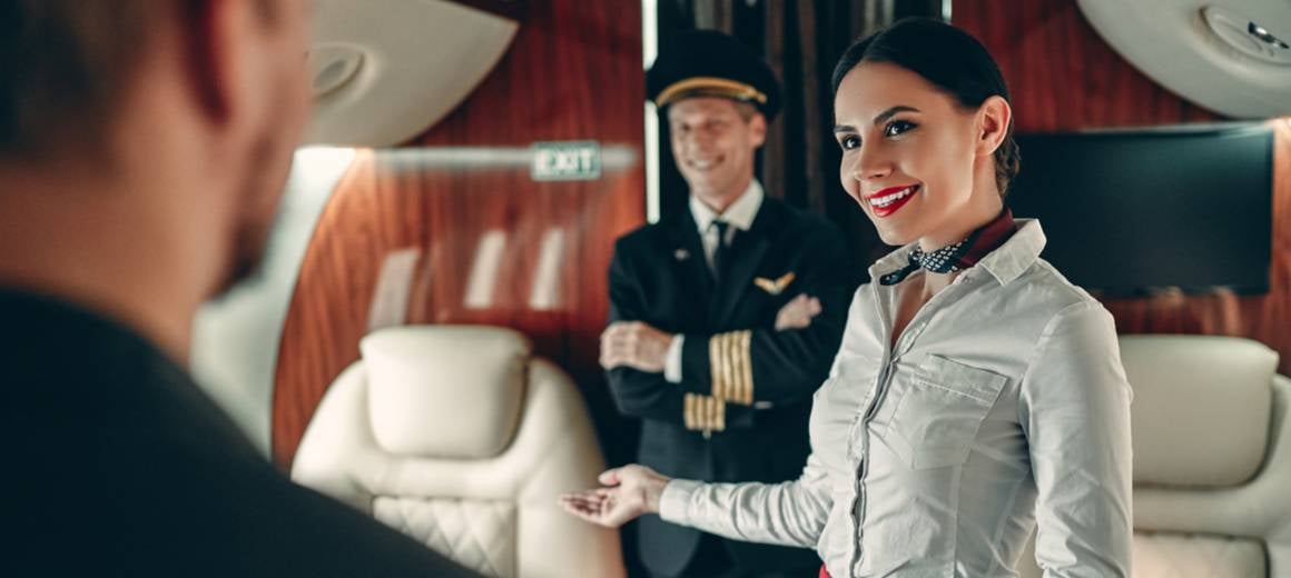 An air hostess and a pilot greet a private jet passenger. 