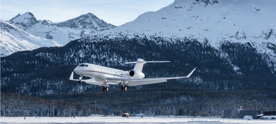 A private jet comes in to land against a backdrop of snow-covered mountains. 