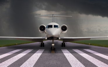 A private jet parked on a runway with storm clouds in the background.