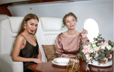 Two women sit at a table inside a luxury private jet.