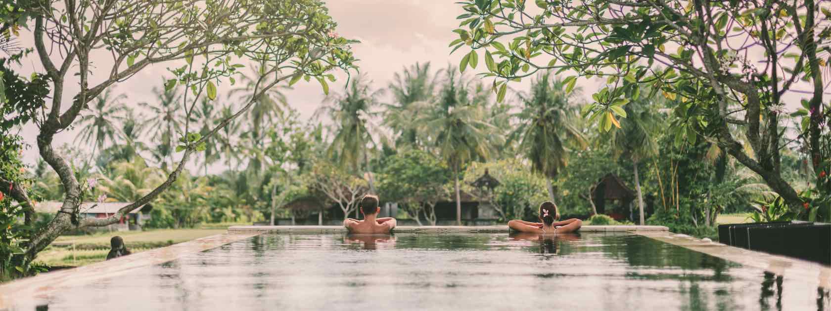 A couple swimming in an infinity pool surrounded by trees in a private villa resort in Ubud, Bali.