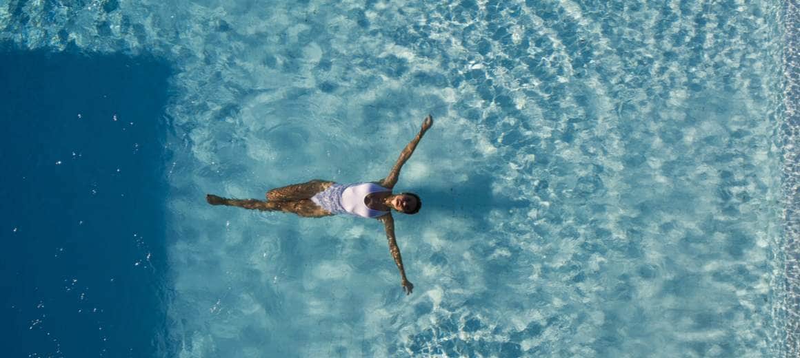 Aerial photo of a woman floating in a swimming pool with arms outstretched.