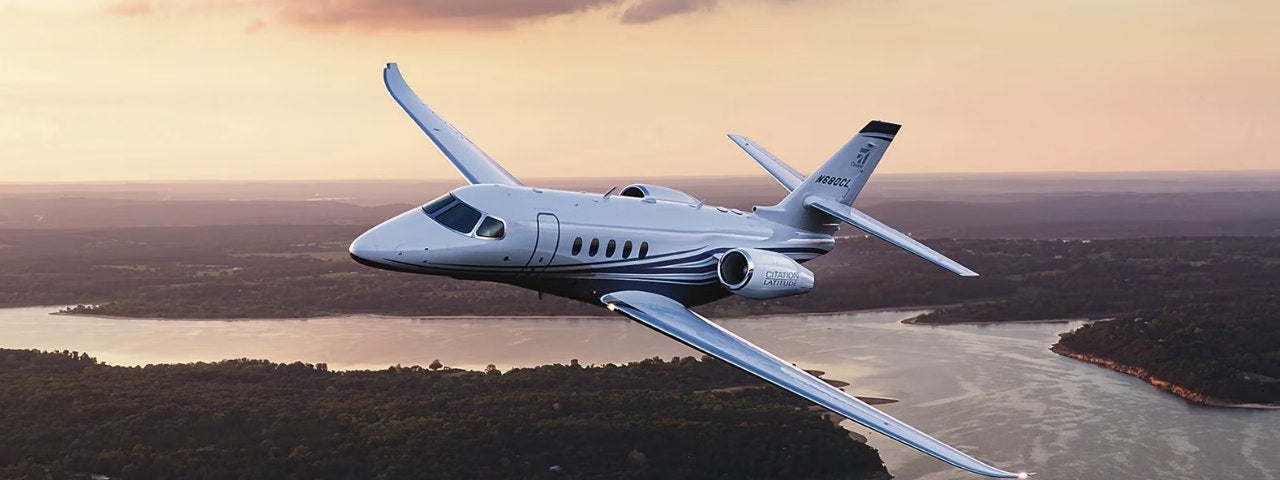 Close-up of a Cessna Citation Latitude flying in the sunset with a river below.