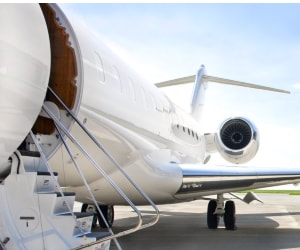 Photo of a modern private jet aeroplane on the tarmac with the door open and stairs leading up to the entrance. 