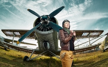 A female pilot stands in front of her airplane.