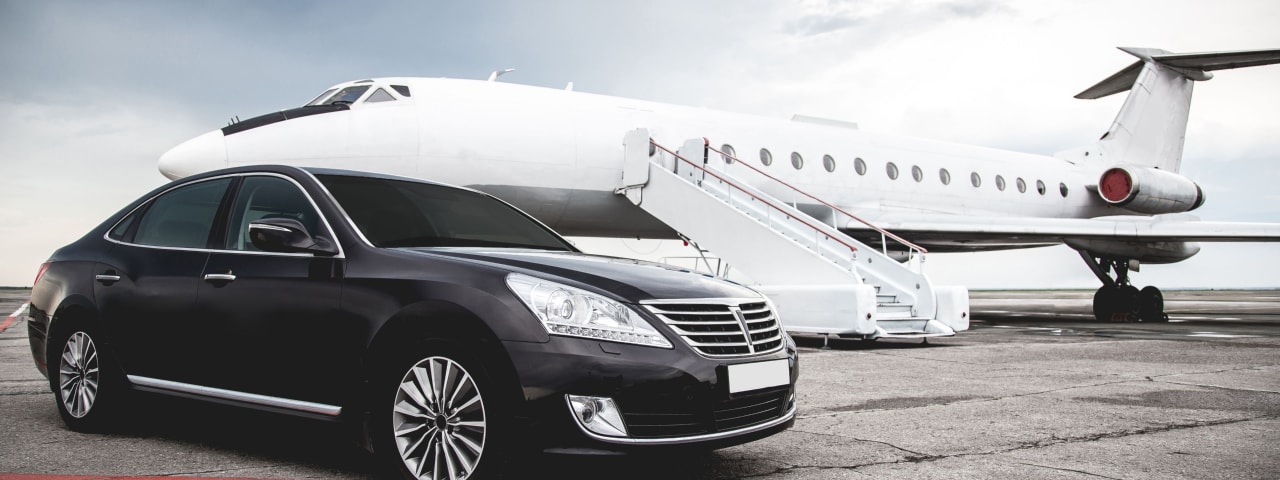 Black car parked in front of a private jet.