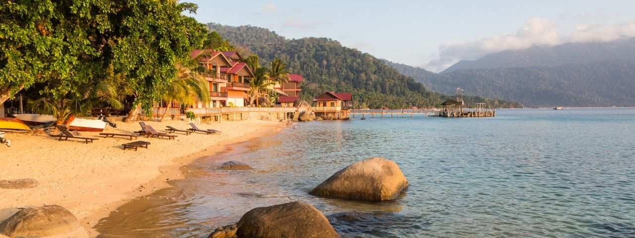 long chairs on a beach with a house in the background in Pulau, Tioman Island in Malaysia