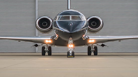 Front view of a black and silver private jet in front of an airport hangar