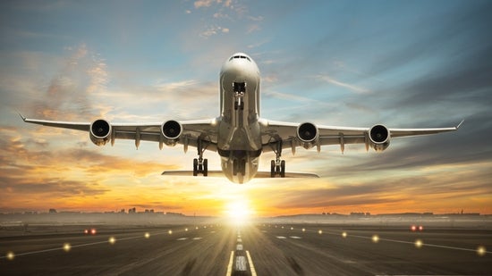 The airplane is taking off with the sunrise in the background