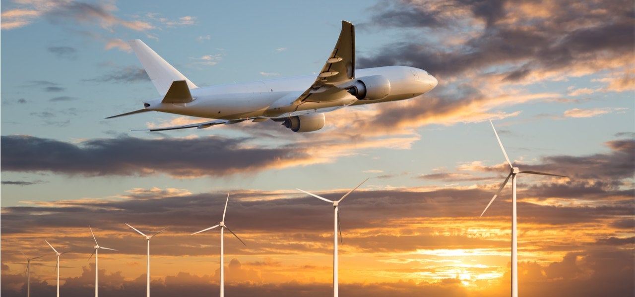 Passenger plane taking off at sunset above wind electric generators