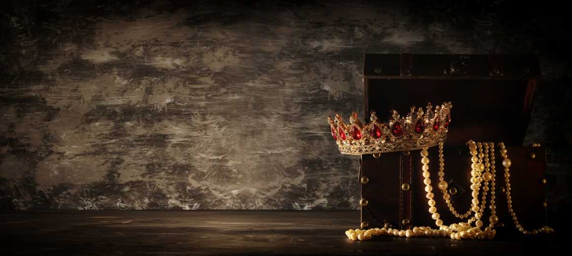 A golden crown of rubies with pearls on the edge of a treasure chest.