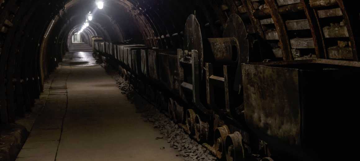 Mining carts in a mine tunnel with lights above them.