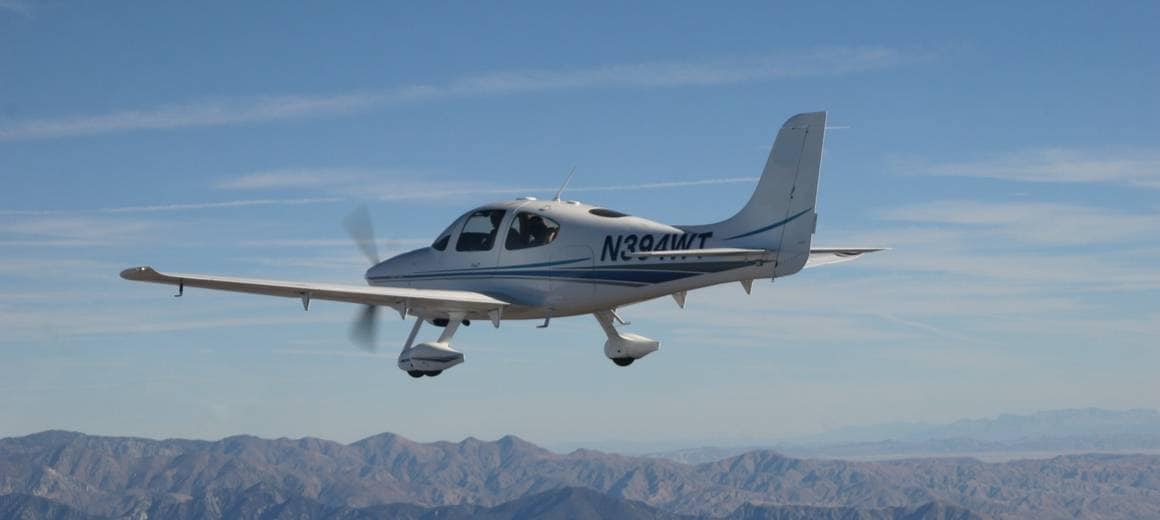 Cirrus SR-22 small private plane flying over mountain range on a sunny day