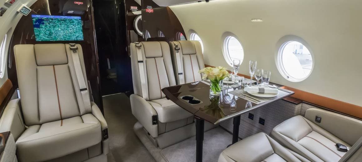 Interior of luxury private jet with grey leather seats and table set for dinner