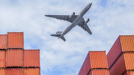 Cargo plane flying over shipping containers.