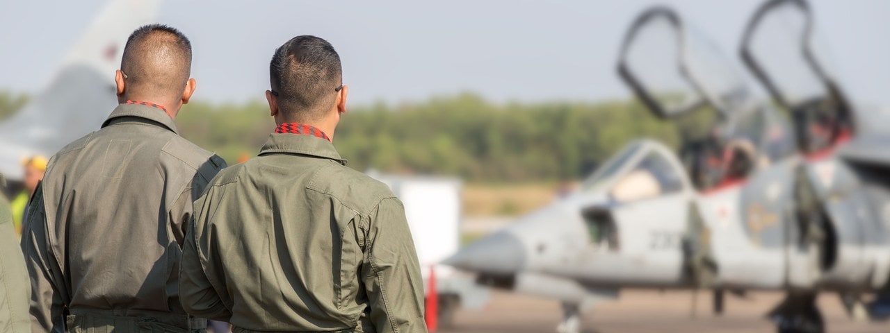 Two military pilots stand near a military jet.