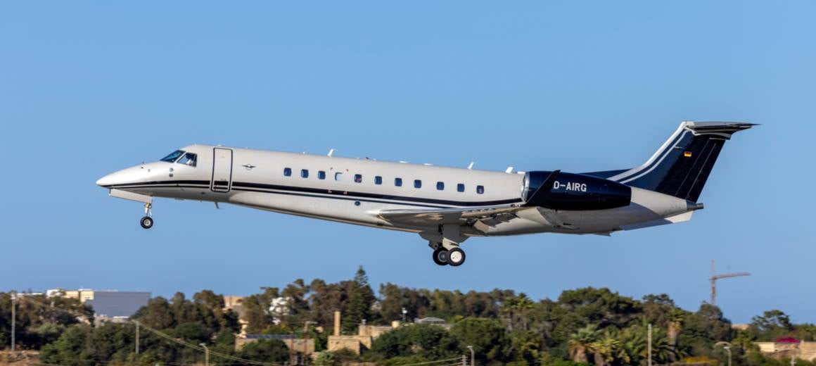 A Blue and White Embraer Legacy 650E on a runway with bright blue skies in the background