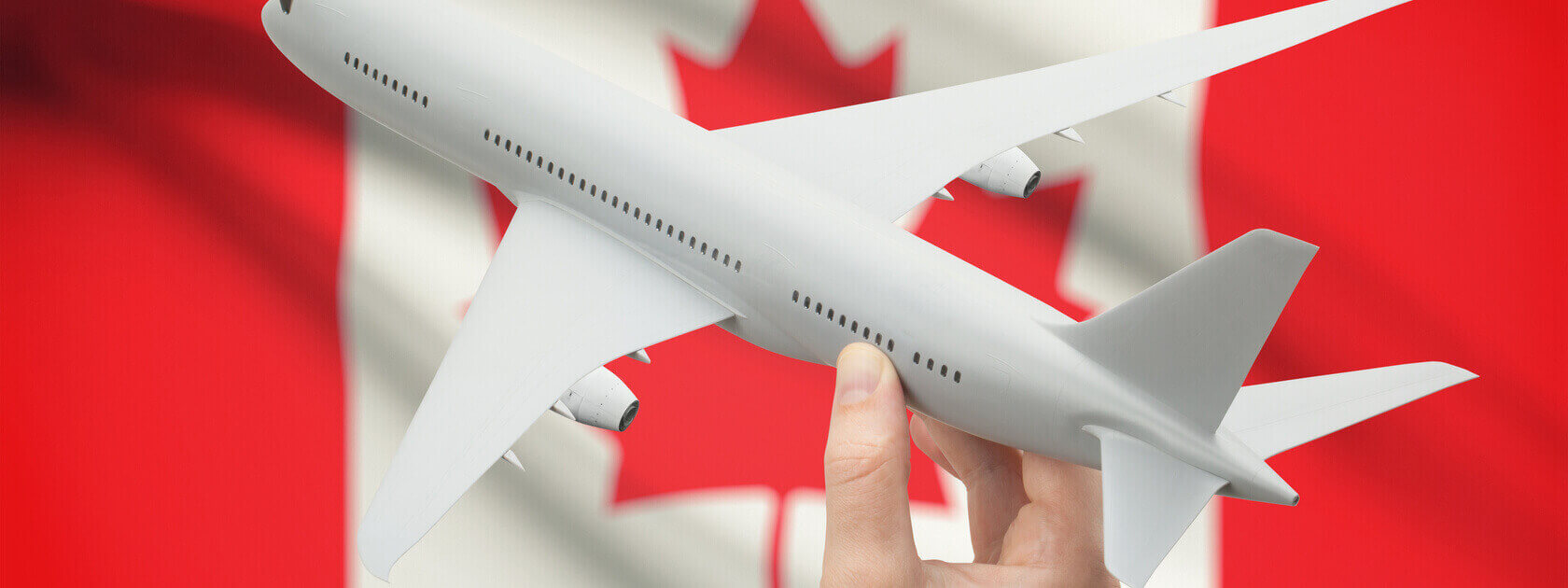 Hand holding plane in front of Canadian flag