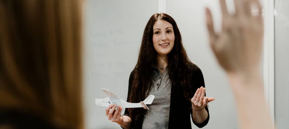 The woman stands in class with an airplne model in her hand