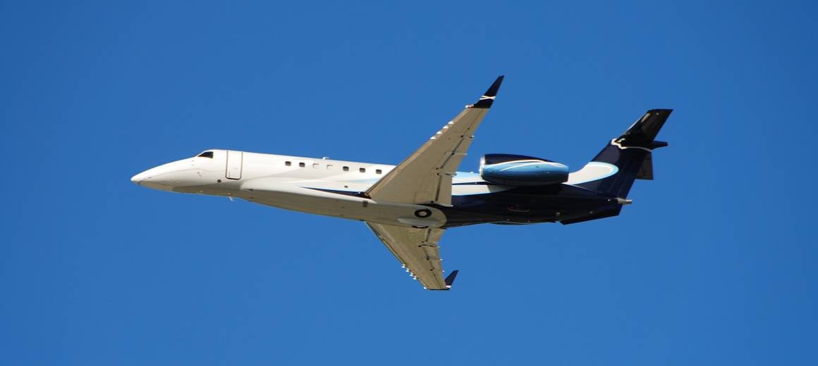 A blue and white Embraer Legacy 650E flying in the bright blue sky