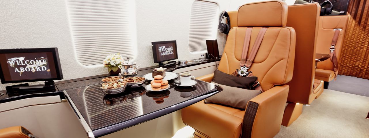 Private plane interior with luxury leather seats and wooden tables holding food