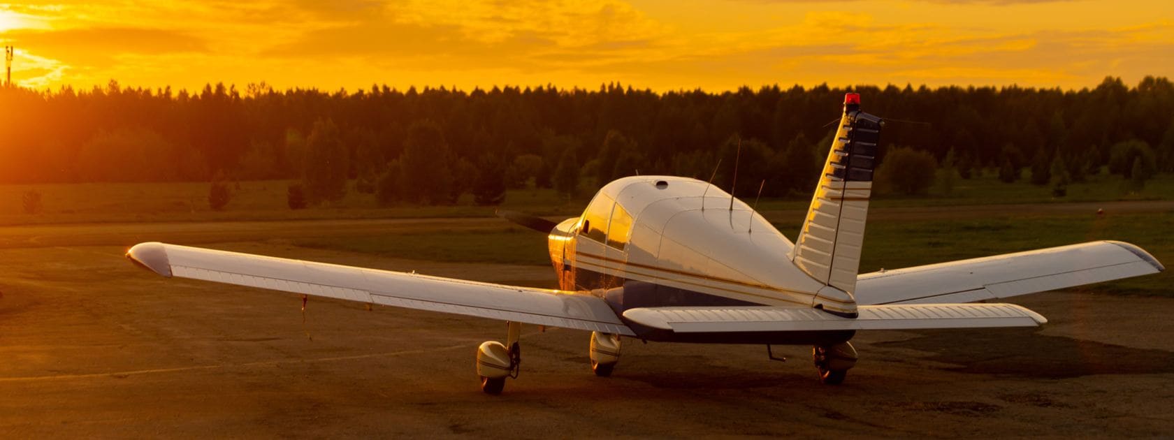 Private jet parked on a runway at sunset, trees in the background.