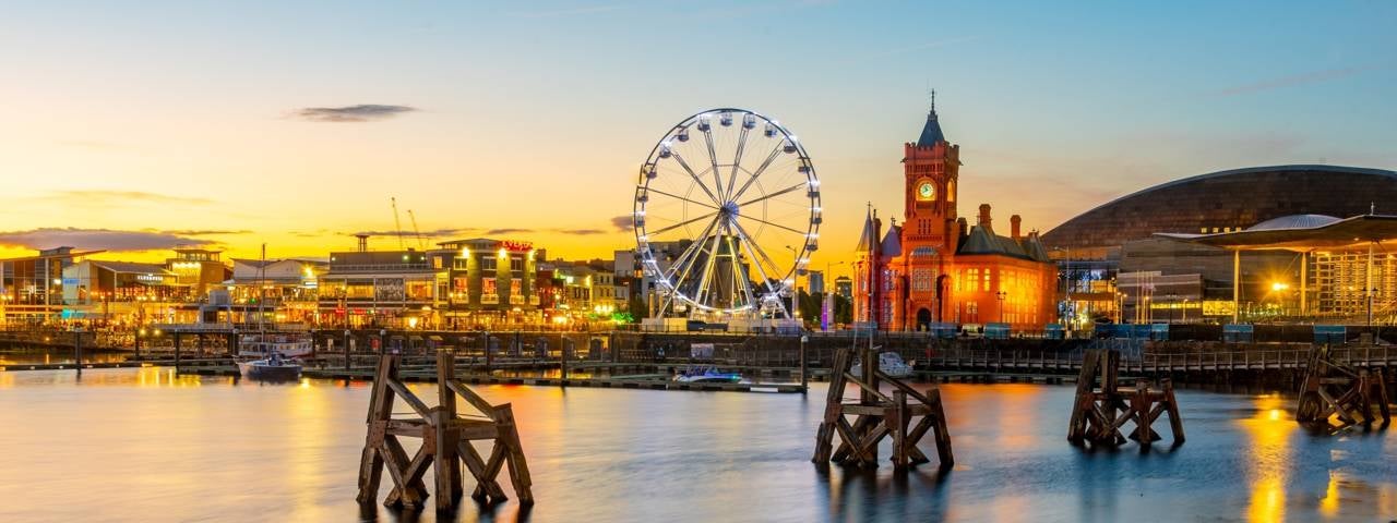 Cardiff Bay at sunset as the buildings and Ferris wheel light up.