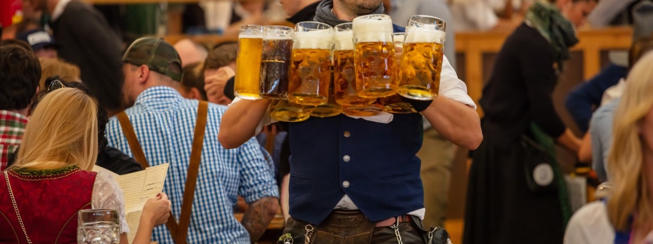 A waiter carrying 10 beer mugs filled with beer.